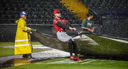 Ejemplar: Jugadores de Piratas de Campeche ayudan a colocar las lonas para cubrir la cancha de Puebla tras intensa lluvia; el juego se aplazó